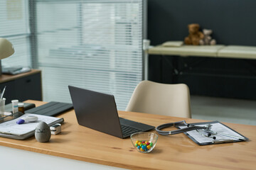 Fototapeta premium Wide shot of medical office desk displaying laptop, stethoscope, clipboard, thermometer, signaling telehealth workflow and patient consultation setup