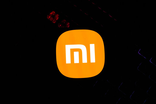 Vibrant Orange Xiaomi Logo Glowing on a Dark Backlit Mechanical Gaming Keyboard Background - Concept for Modern Consumer Electronics, Tech Innovation, and Global Smartphone Branding Trends