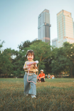 Adorable little Southeast Asian toddler girl playing with a pink water gun toy in a city park during Songkran festival. Happy child in traditional outfit enjoying summer outdoor fun with family