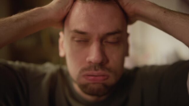 Close up portrait shot of desperate adult man covering face with hands going through emotional breakdown while sitting indoors, video effect