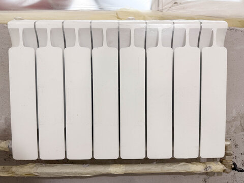 Installation of heating and water supply systems. White heating radiator and pipe outlets on a concrete wall for plumbing. Protective film and masking tape on communications.