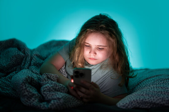 Kid lying in bed with phone at night. Teenager using smartphone in bed at night.