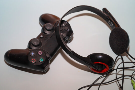 Lviv, Ukraine - March 19, 2026: A black DualShock 4 controller and a wired headset with a microphone lie on a light surface with a subtle blue tint. This set of gaming peripherals demonstrates the ess