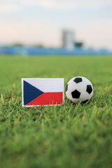 Fototapeta premium Czech Republic national flag and football on grass field with soft blurred stadium background, representing European football ambition, unity, and competitive sports identity.