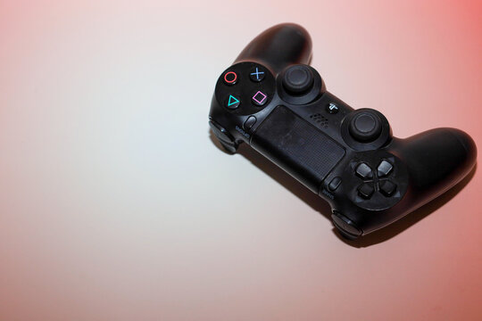 Lviv, Ukraine - March 19, 2026: ​A black wireless DualShock controller is positioned at an angle on a light background with soft pink lighting.