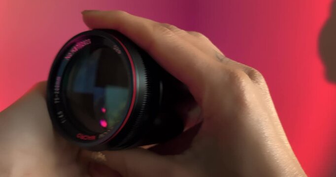 A person uses both hands to display a classic vintage MC zoom lens against a pink backdrop. Macro shot highlighting the retro build, glass reflections, and manual zoom ring.