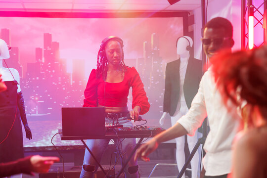 Woman dj using mixer console to blend tracks on stage at nightclub disco party. African american musician in headphones pressing buttons on electronic music station at club
