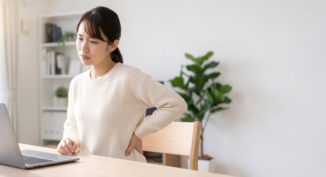 Japanese woman suffering from lower back pain while working on laptop with copy space