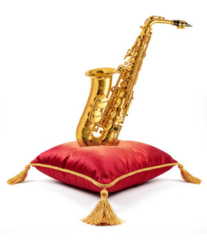 Złoty saksofon na czerwonej poduszce kr&oacute;lewskiej ze złotymi frędzlami