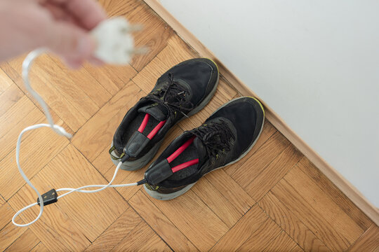 Male shoes with electric dryer on floor indoors, closeup photo. Drying wet sneakers using plug-in electric shoe dryer, home interior scene
