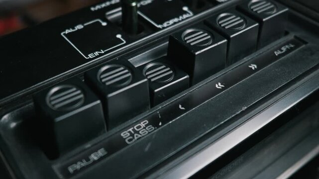 A detailed close-up shows a finger pressing the play button on a vintage black tape recorder. Concept of nostalgia, retro technology, analog audio, and listening to music from the past.