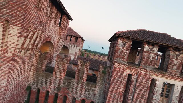FPV drone flight over brick battlements and towers of medieval Rocca Sforzesca fortress in Soncino, Italy. Aerial forward tilting