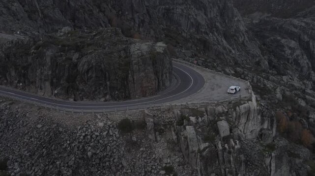 EN339 iconic hairpin near Torre in Serra da Estrela Seia municipality Guarda district Centro region Portugal with parked car on cliff edge terrace and steep granite escarpment, drone establishing shot