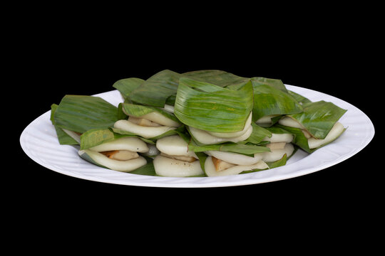 Vietnamese traditional round sticky rice cake (Banh Nep) with meat filling wrapped in banana leaves on a white plate isolated on black transparent background.