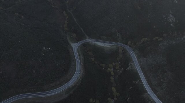 EN339 mountain road in Serra da Estrela Seia municipality Guarda district Centro region Portugal showing tight switchback geometry carved into slope with sparse vegetation, top down drone descent shot
