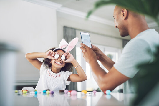 Dad, child and bunny ears with phone photography for love, bonding or easter holiday together. Man, girl and tech in house with silly face, laugh and candy eggs for vacation and festive memories