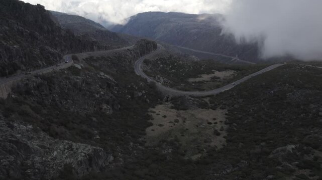 EN339 mountain road near Torre in Serra da Estrela Seia municipality Guarda district Centro region Portugal crossing subalpine rocky terrain with orographic cloud cover, aerial drone glide shot