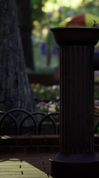 In a park, people are enjoying their time near a water fountain. Trees surround the area while flowers are visible on the ground. It is daylight and activity is happening.