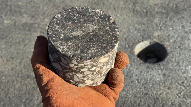 Hand in protective glove holding a core sample of asphalt taken from a road surface