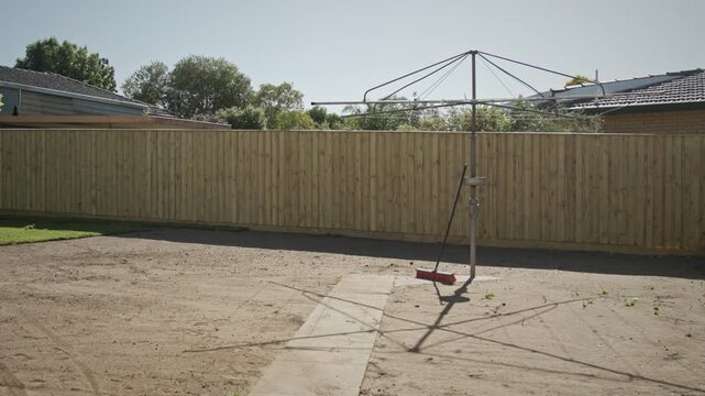 A suburban backyard featuring a newly installed light timber fence, with a classic rotary clothesline (Hills Hoist) standing centrally.