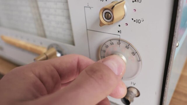 A person turns the main tuning dial on a piece of vintage analog electronic test equipment. Concept of retro engineering, electronic calibration, scientific measurement, and analog signal.