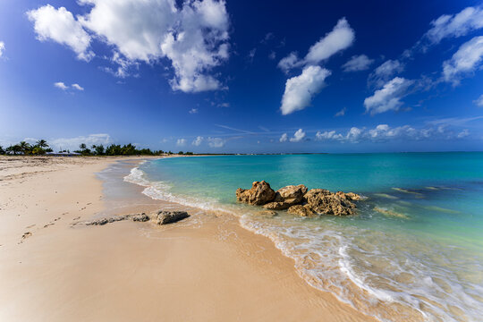Crystal-clear turquoise water gently washing over a sandy beach with rocks and soft waves in Treasure Cay, Great Abaco, Bahamas - an idyllic Caribbean coastline