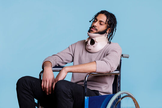 Arab man wearing cervical collar and sleeping while sitting in wheelchair. Young exhausted patient with closed eyes recovering from accident, using neck brace for spinal protection