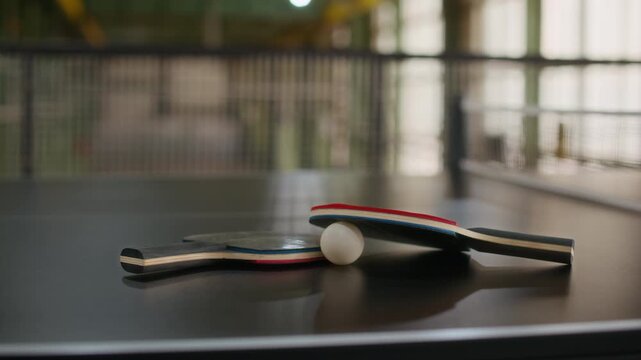 Close up shot of two table tennis paddles and white ball resting on ping pong table near net