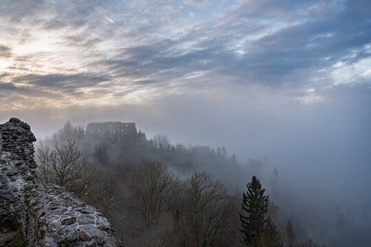View from Medieval Wall over Foggy Valley towards Eisenberg Castle Ruins Shrouded in Mist at Dawn, Atmospheric Mountain Landscape with Ancient Stone Fortress, Allgaeu Alps, Germany