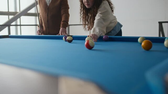 Medium shot of Caucasian couple chatting during pool game while woman aiming and making her move with cue at blue billiard table
