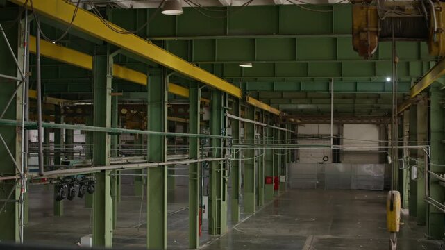 Wide establishing shot of empty industrial loft interior with crane hoist, green steel columns, overhead beams, large open floor space and modern urban warehouse atmosphere