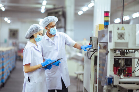 Factory workers analyze machine performance while documenting results on clipboard. Concept represents monitoring, evaluation, and quality control in industrial production line.