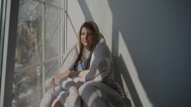 A woman sits on the windowsill and squints from the sun