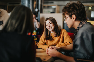 Naklejka premium Students sit around a table smiling and talking while studying together. A casual group of young friends engages in a relaxed conversation and collaborative study session.