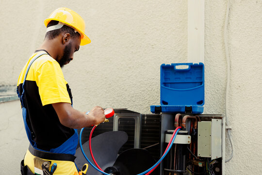 Proficient african american worker doing routine condenser maintenance, assembling manifold indicators before starting work. Qualified electrician getting equipment ready to check freon leaks
