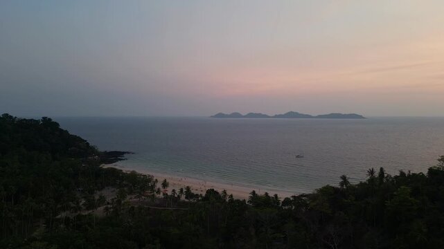 Koh Mook, Thailand: Cinematic aerial drone footage of the sunset over Koh Muk with the Kradan island in the background in Thailand. Shot with a forward motion above palm tree lining Charlie beach