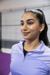 Obraz premium Indian adult woman standing and posing in sports facility with purple court and quarter-zip top