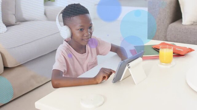 Vertical video: Boy tapping tablet at table, causing floating colorful circles for education app