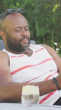 Vertical video: Reacting to zoom man in tank on chair smiling into laughing in garden shades, glass