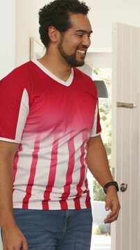 Vertical video: Walking man in red tee bringing green cans at entry after door opening greeting pal