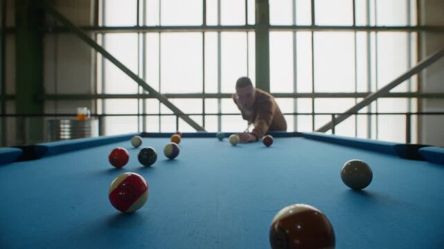 Stab shot of young Caucasian man focusing and aiming cue ball before taking shot at billiards table in indoor setting, showing concentration and leisure activity