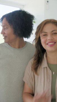 Two friends side-by-side raising pink mug toward camera, third joining, celebrating in kitchen
