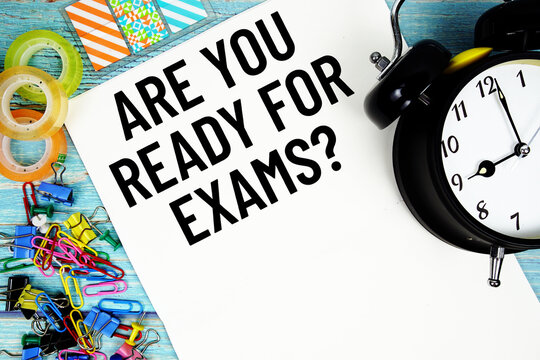 Are You Ready For Exams? text with alarm clock and colorful office supplies on a blue wooden surface