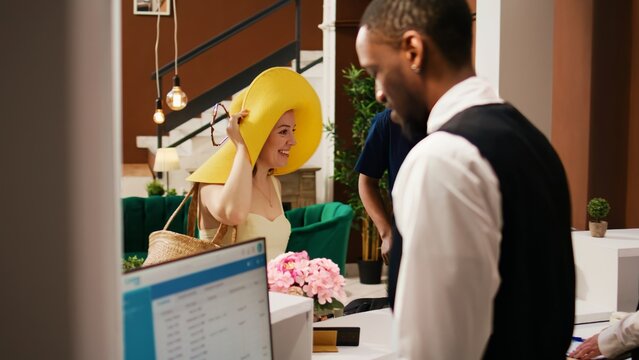Diverse couple arriving at hotel reception to do check in process for summer holiday at modern resort. Travellers preparing to see room and enjoy honeymoon vacation trip. Handheld shot.