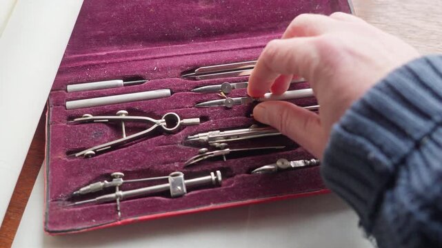 POV shot of a hand choosing a tool from a drafting set, capturing decision-making and preparation in a precise design process.