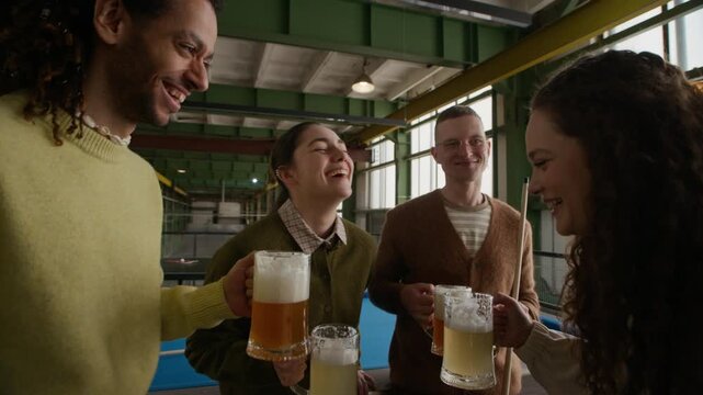 Medium shot of four diverse friends holding beer mugs and toasting while standing near pool table in indoor leisure setting