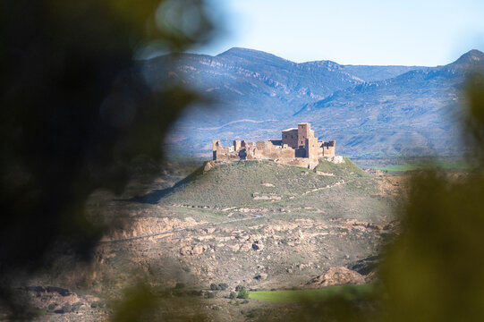 Montearagon Castle ruins on a hilltop near Huesca, Spain, medieval fortress silhouette against the Pre-Pyrenees mountains and blue sky, historic landmark in Aragon landscape at sunset.