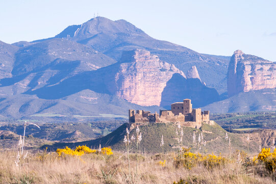 Montearagon Castle ruins on a hilltop near Huesca, Spain, medieval fortress silhouette against the Pre-Pyrenees mountains and blue sky, historic landmark in Aragon landscape at sunset.