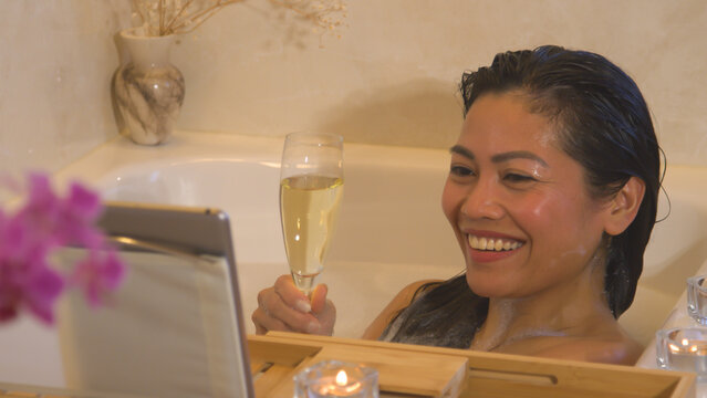 CLOSE UP Smiling young lady in bubble bath having a romantic date via video call