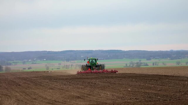 Tractor pulling a planter machine across a plowed field, seeding crops under a cloudy sky in spring